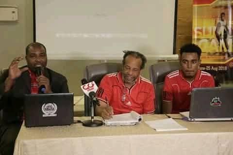 Coach Carlos speaking alongside colleagues during a sports press conference
